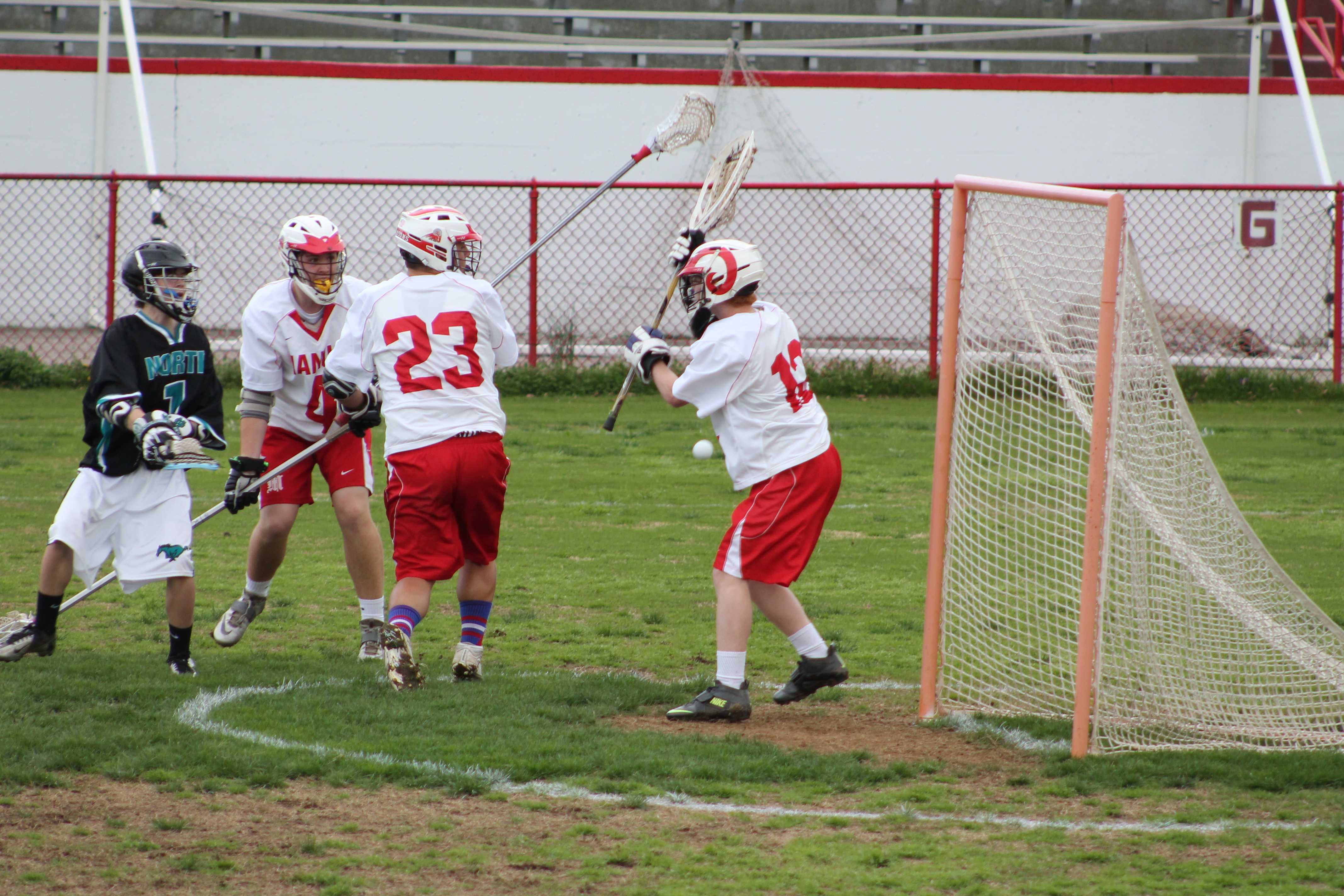 Goalie John Biggs (12, #12) prepares to block a shot on goal with his net. However, the ball instead hit Biggs in the side and missed the goal.