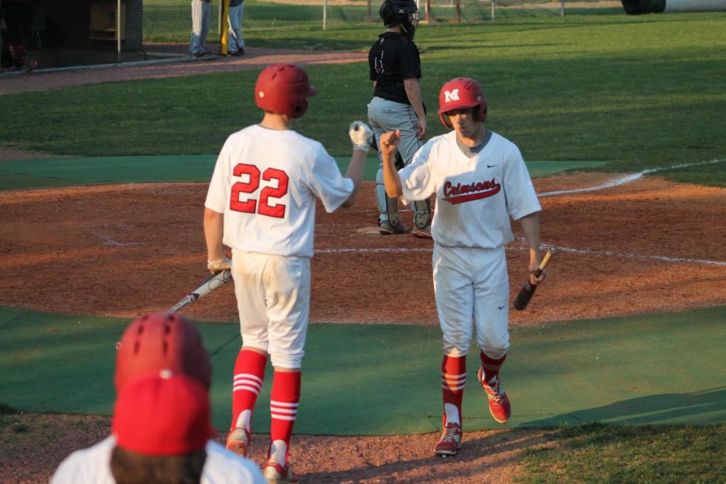 Evan Dilbeck (11, #13) celebrates with teammate Sam Clinard (11, #22) after scoring off of a hit by Ben Cooper (12, #32). The score gave Manual its first lead of the game at 3-2.