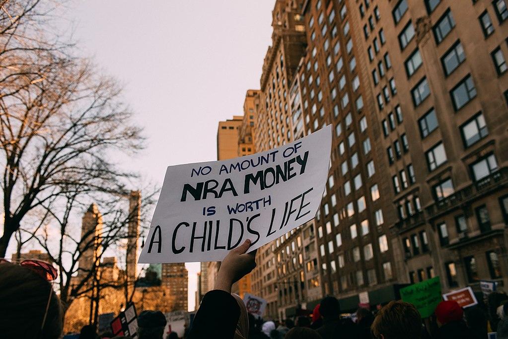 Photo of a sign at a March For Our Lives protest. Photo by Tristan Loper on Flickr, licensed under CC BY-SA 2.0. No changes were made to the original image. Use of this image does not indicate photographer endorsement of this article. Image link: https://www.flickr.com/photos/129094836@N03/40993495701