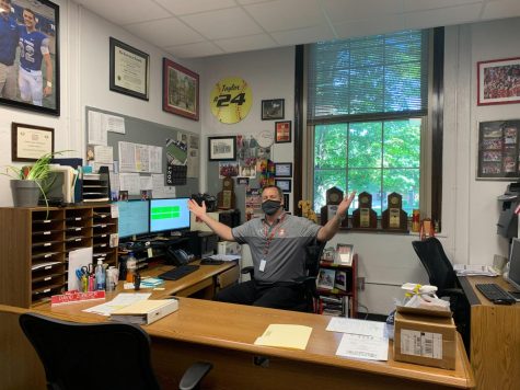 Athletic Director David Zuberer holds his arms out to welcome people to buy spirit wear in his office