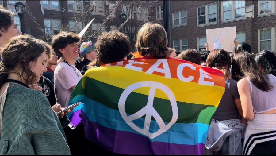 students drapes themselves in a pride flag while listening to speakers. Photo by Cassidy Overberg