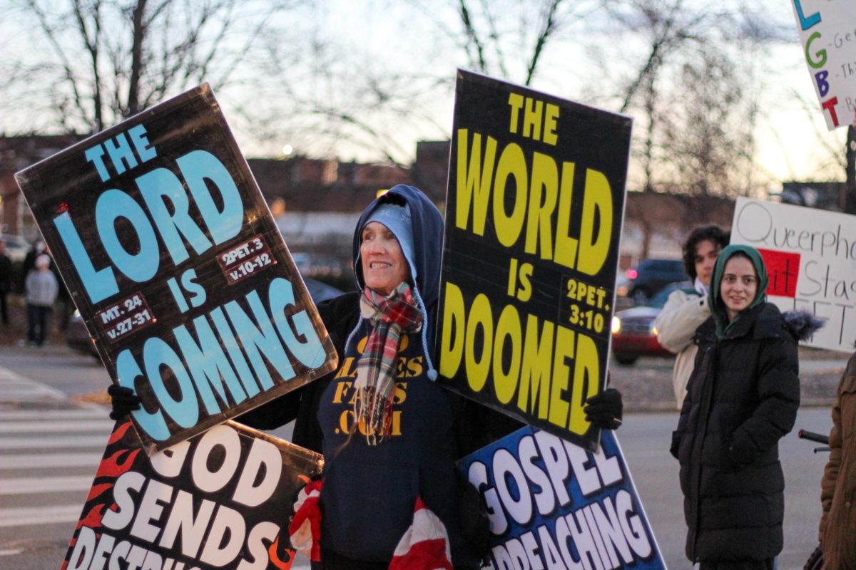 A member of the Westboro Baptist Church holding multiple signs with different phrases.