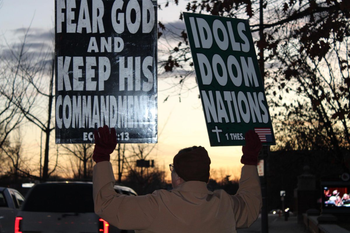 A member of the Westboro Baptist Church holding signs as cars pass by.