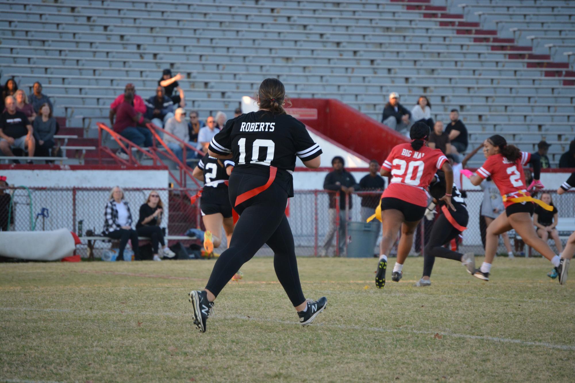 The senior teams' quarterback Riley Roberts (#10, 12) runs down the field, watching a play off to the side.