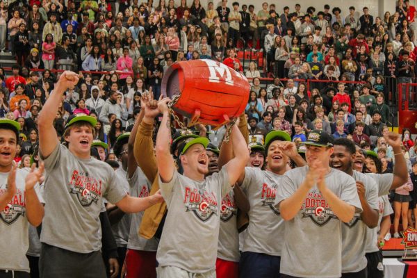 The football team walks around the gym floor, holding the barrel. 