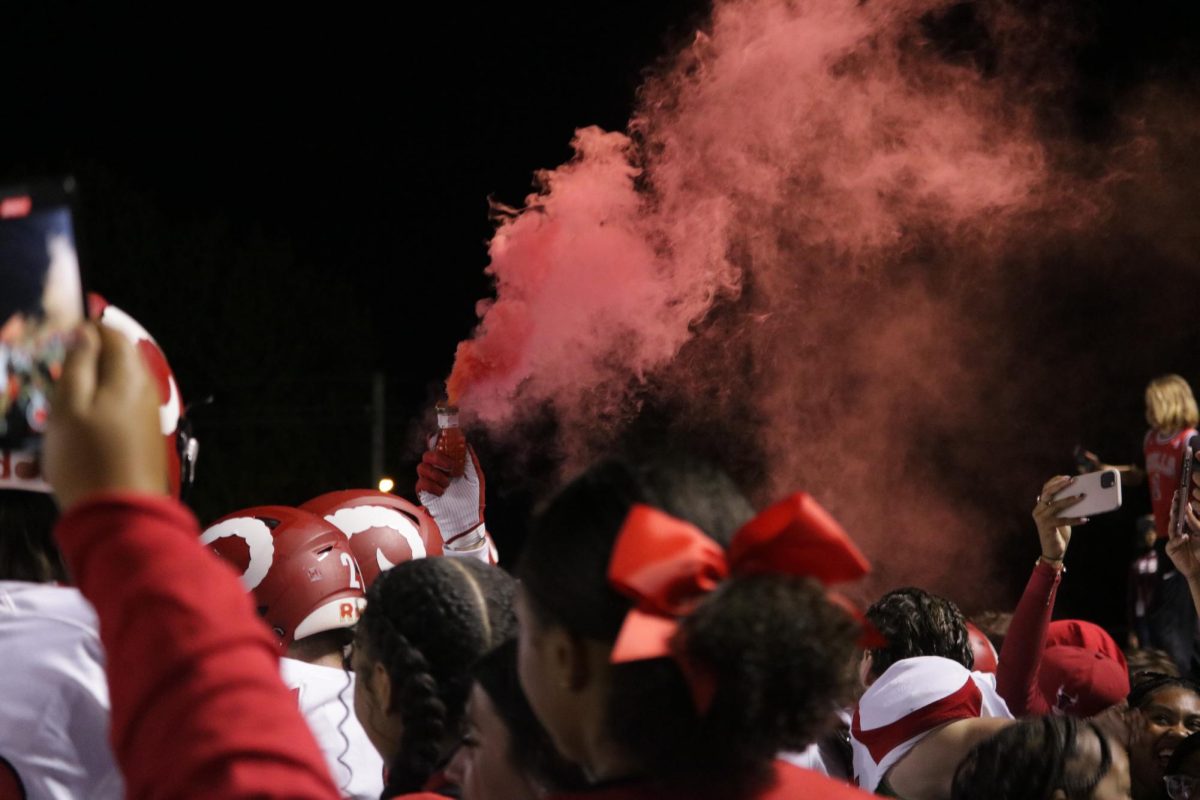 Football players, cheerleaders, students and fans alike celebrate Manual's win, with a player holding a red smoke bomb in hand. 